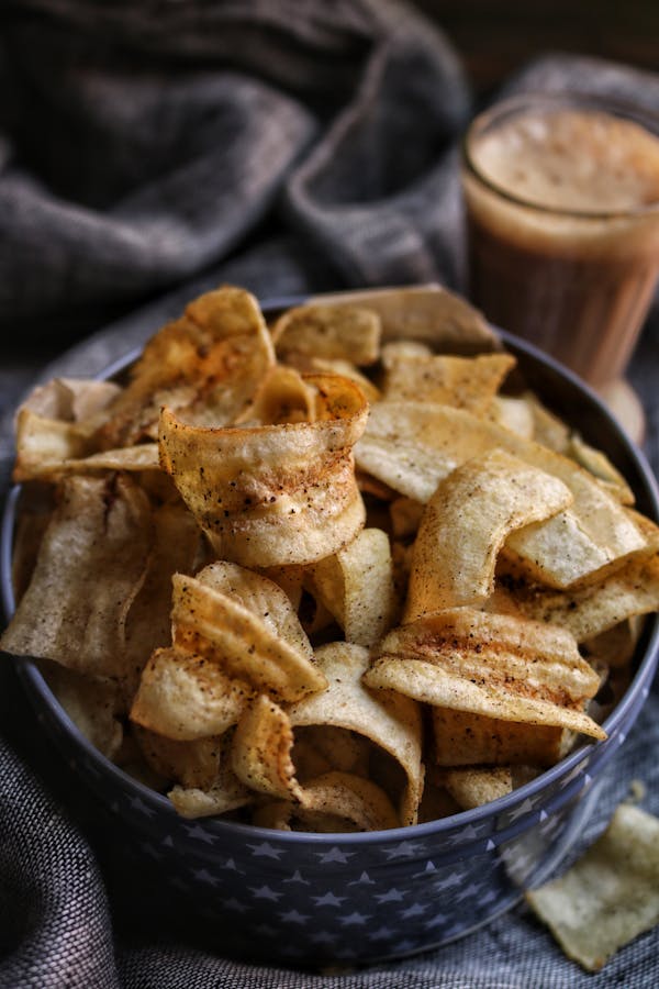 A bowl of delicious homemade banana chips paired with a refreshing drink, perfect for a tasty snack.