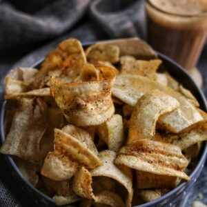 A bowl of delicious homemade banana chips paired with a refreshing drink, perfect for a tasty snack.